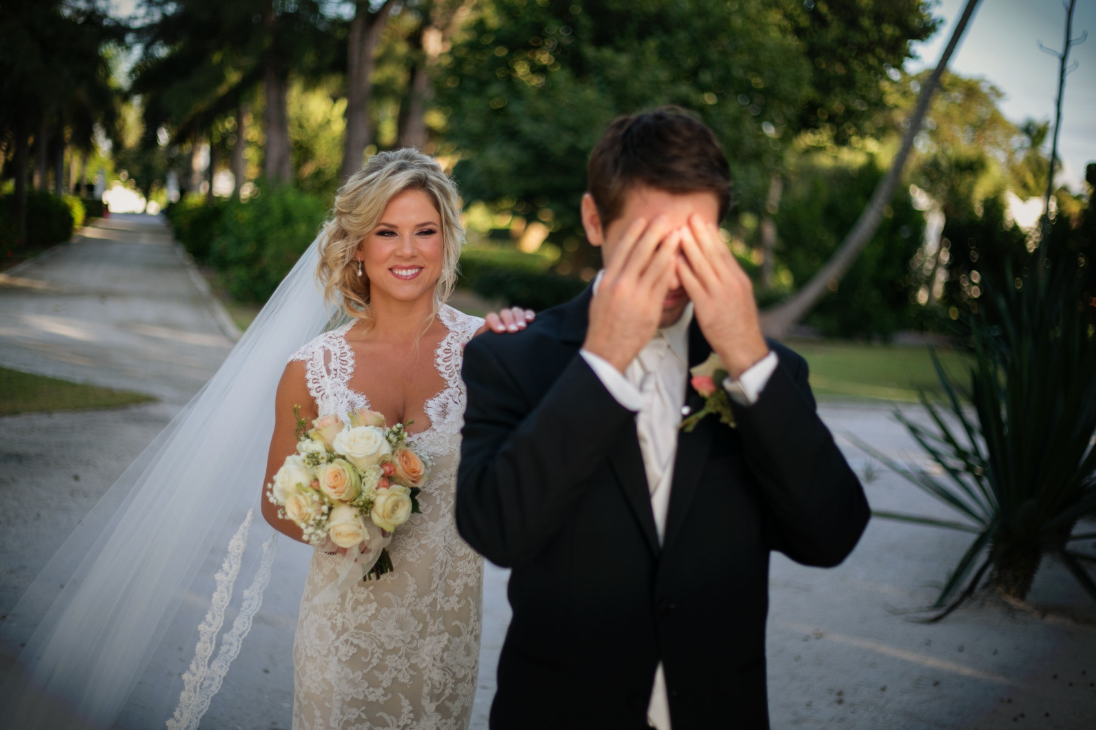 groom covers eyes as bride approaches him from behind for first look